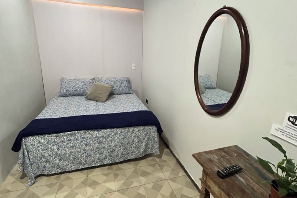 A bedroom with a bed, a wooden bench, a mirror, and a potted plant.