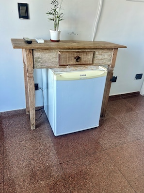 A compact kitchenette with a fridge, a wooden countertop, a potted plant, and a wall-mounted light switch.