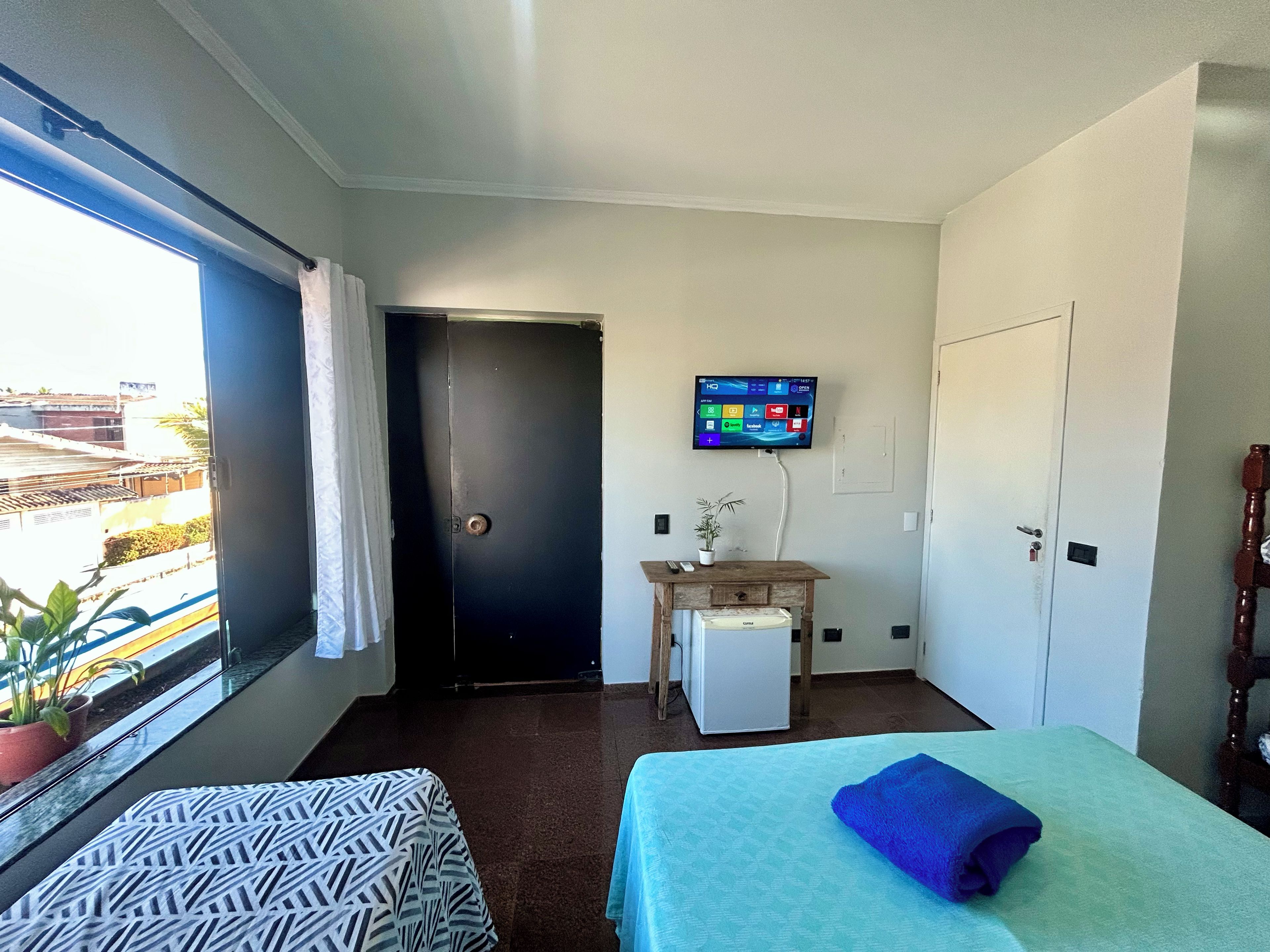 A hotel room with a bed, a small desk, a television mounted on the wall, and a window with curtains.
