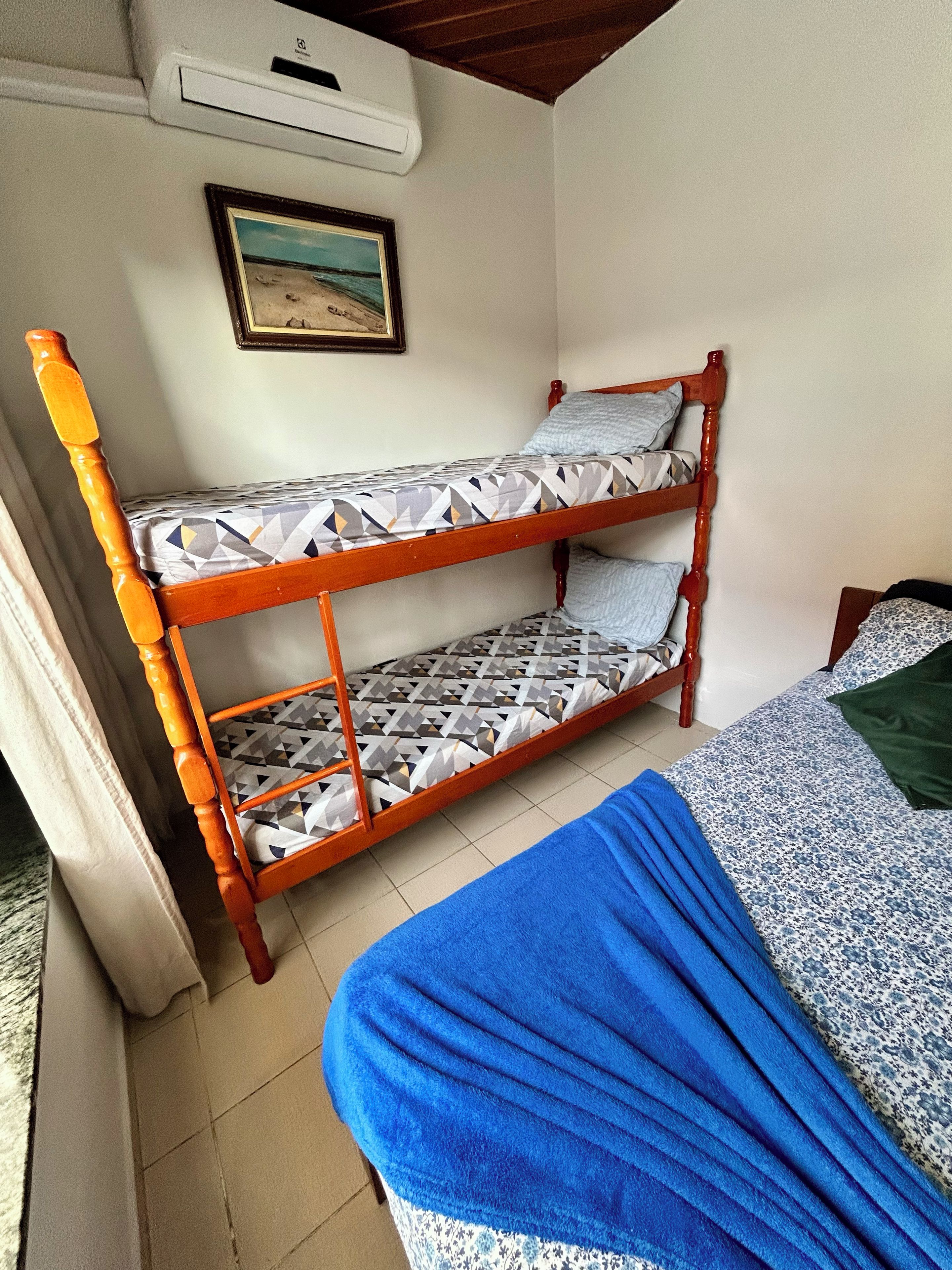 Una cama litera con ropa de cama estampada, una colcha azul, un cuadro en la pared y un equipo de aire acondicionado.