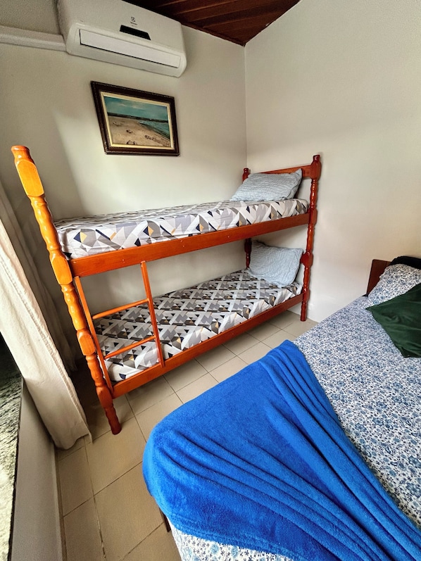 A bunk bed with patterned bedding, a blue blanket, a framed picture on the wall, and an air conditioning unit.