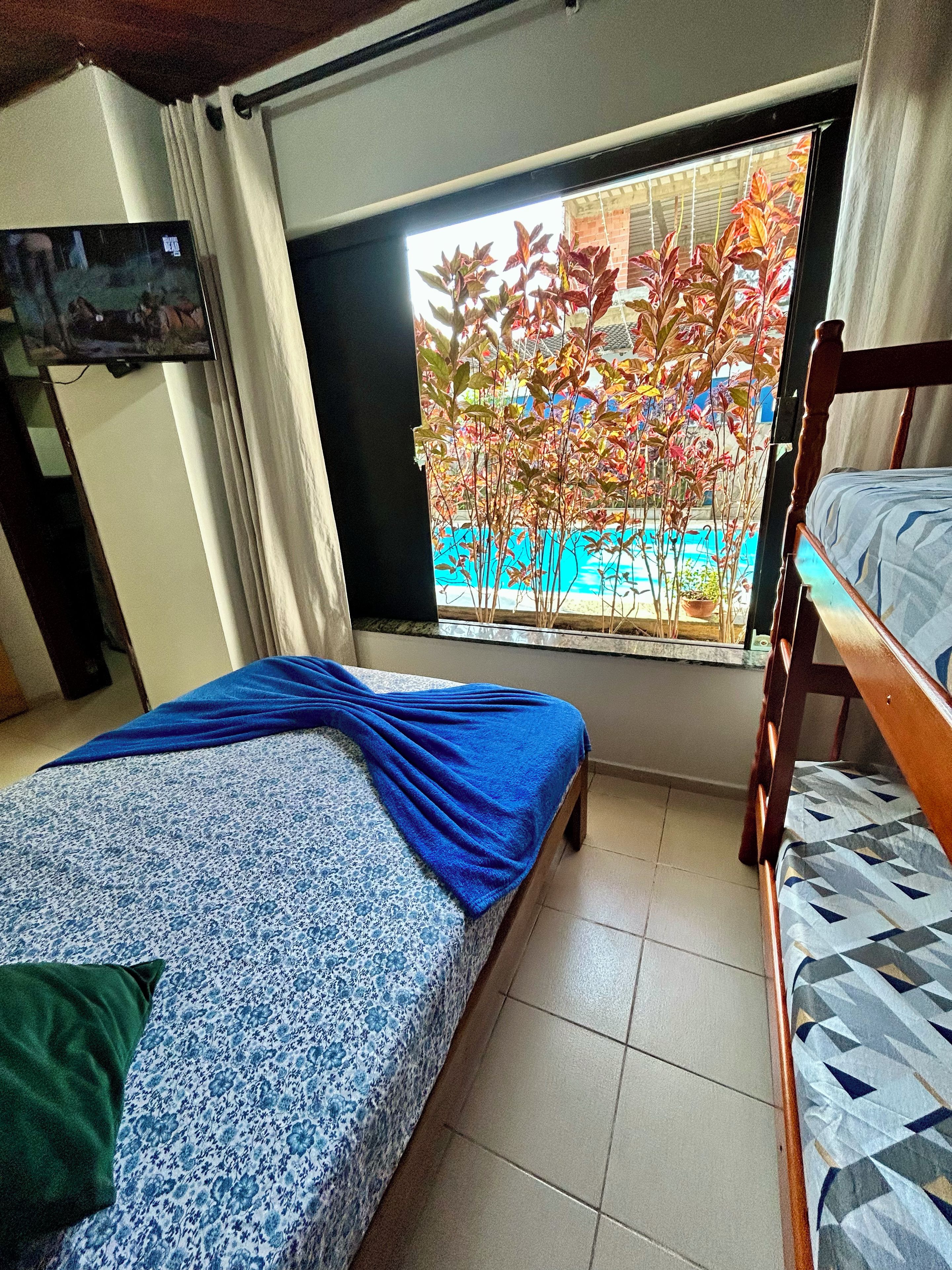 A bedroom with a bed, a window with a view of trees, a TV, and a bunk bed.