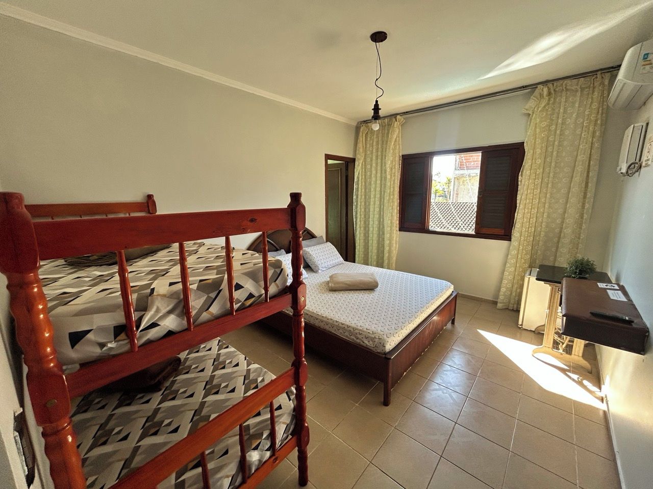 A bedroom with a bunk bed, a single bed, a desk, and a window with curtains.