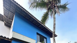 Een blauw gebouw met een balkon, een bankje en een palmboom.
