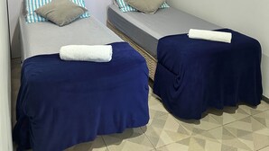 Een kamer met twee éénpersoonsbedden, elk met een blauwe spreidek en een witte handdoek.