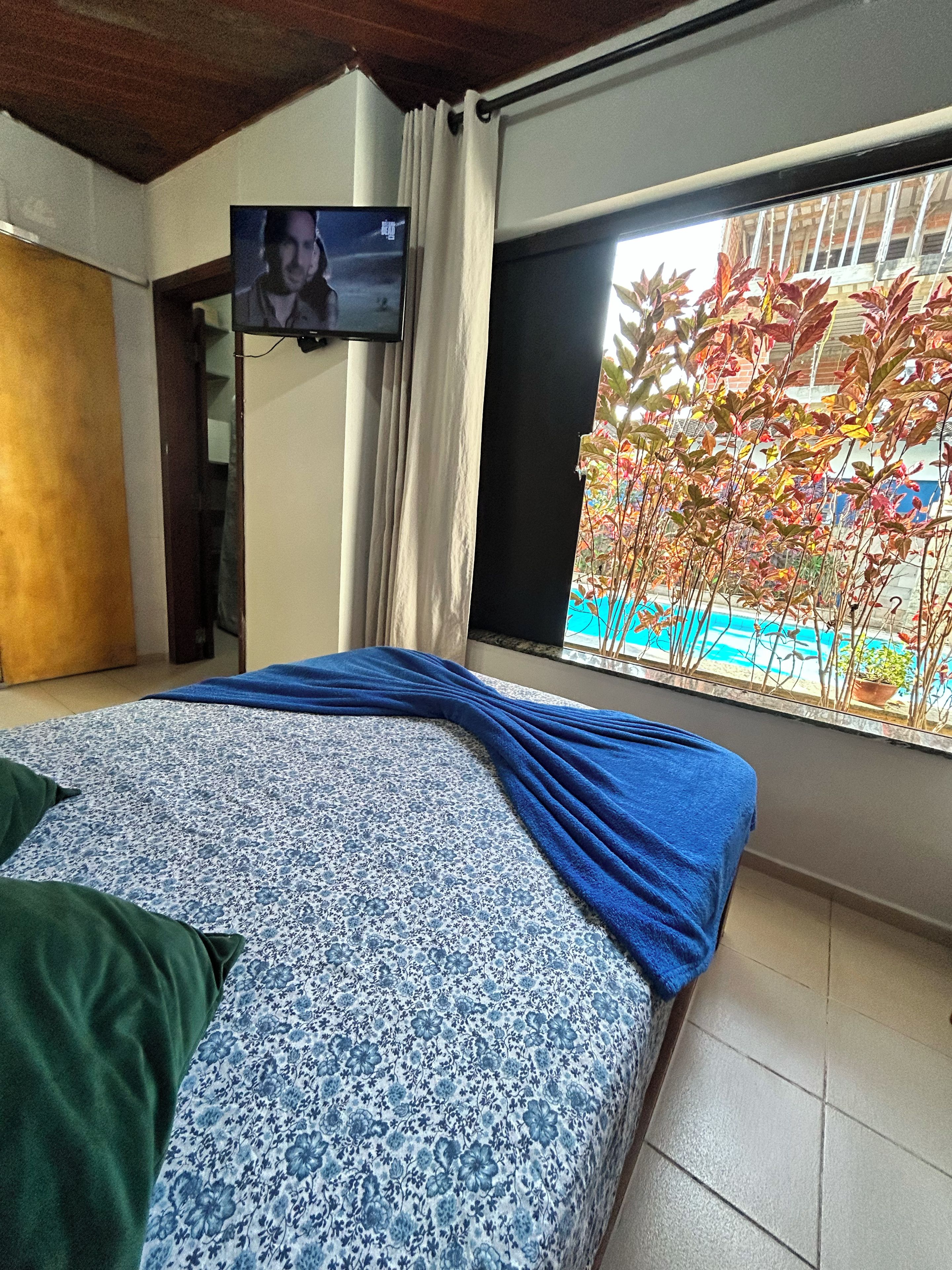 Un dormitorio con cama, televisión, ventana con vista a árboles y puerta.