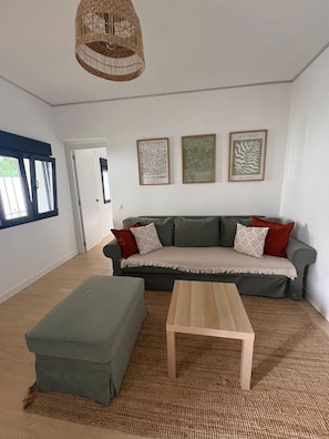 A living room with a sofa, ottoman, and a hanging light fixture. There are framed artworks on the wall. - Benalbali Beach House, Benalmádena Costa, 200 m from the beach (Benalmádena)