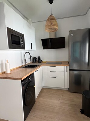 A modern kitchen with a built-in microwave, a stainless steel refrigerator, a washing machine, and a flat-screen TV. - Benalbali Beach House, Benalmádena Costa, 200 m from the beach (Benalmádena)