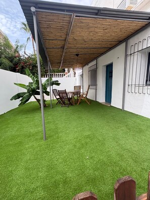 A covered patio area with artificial grass, a table with chairs, and a blue door. - Benalbali Beach House, Benalmádena Costa, 200 m from the beach (Benalmádena)