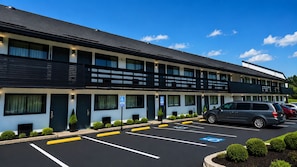 Un hôtel à plusieurs étages doté d’un parking, de places de stationnement accessibles aux personnes handicapées et d’un véhicule stationné sur le parking.