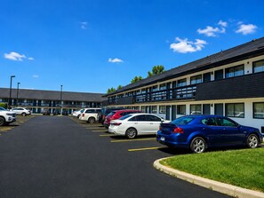 Un parking où plusieurs voitures sont garées devant un bâtiment doté d’un toit plat et d’une rangée de fenêtres.