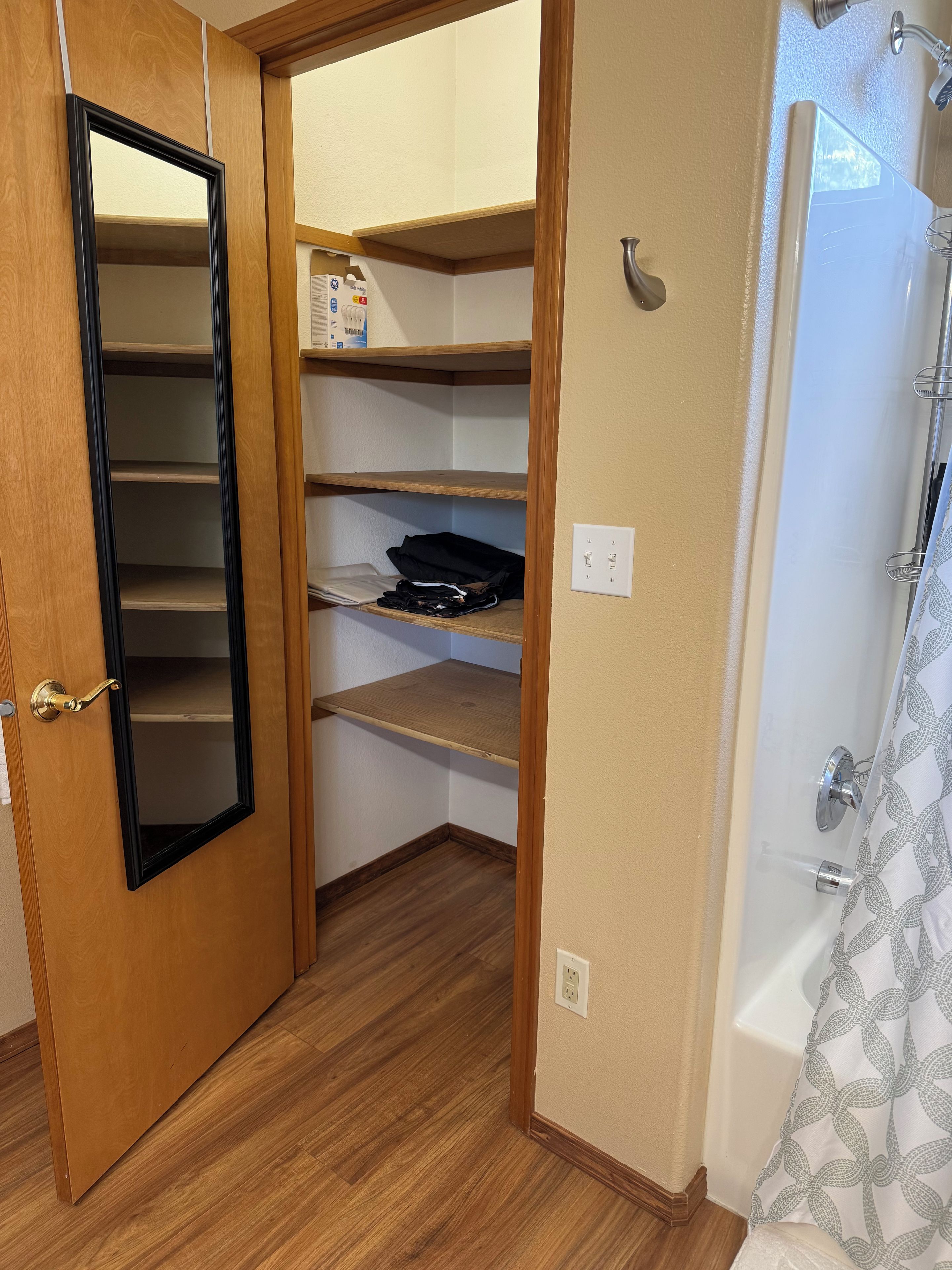 Un vestidor con estantes de madera, una puerta con tirador de latón y una zona de ducha con cortina estampada.