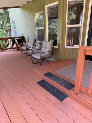 A covered porch with wooden flooring, outdoor seating, and potted plants.