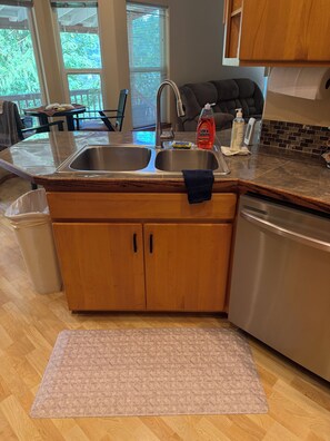 Una cocina con un lavamanos doble, armarios de madera, un refrigerador de acero inoxidable y una alfombra estampada en el suelo.