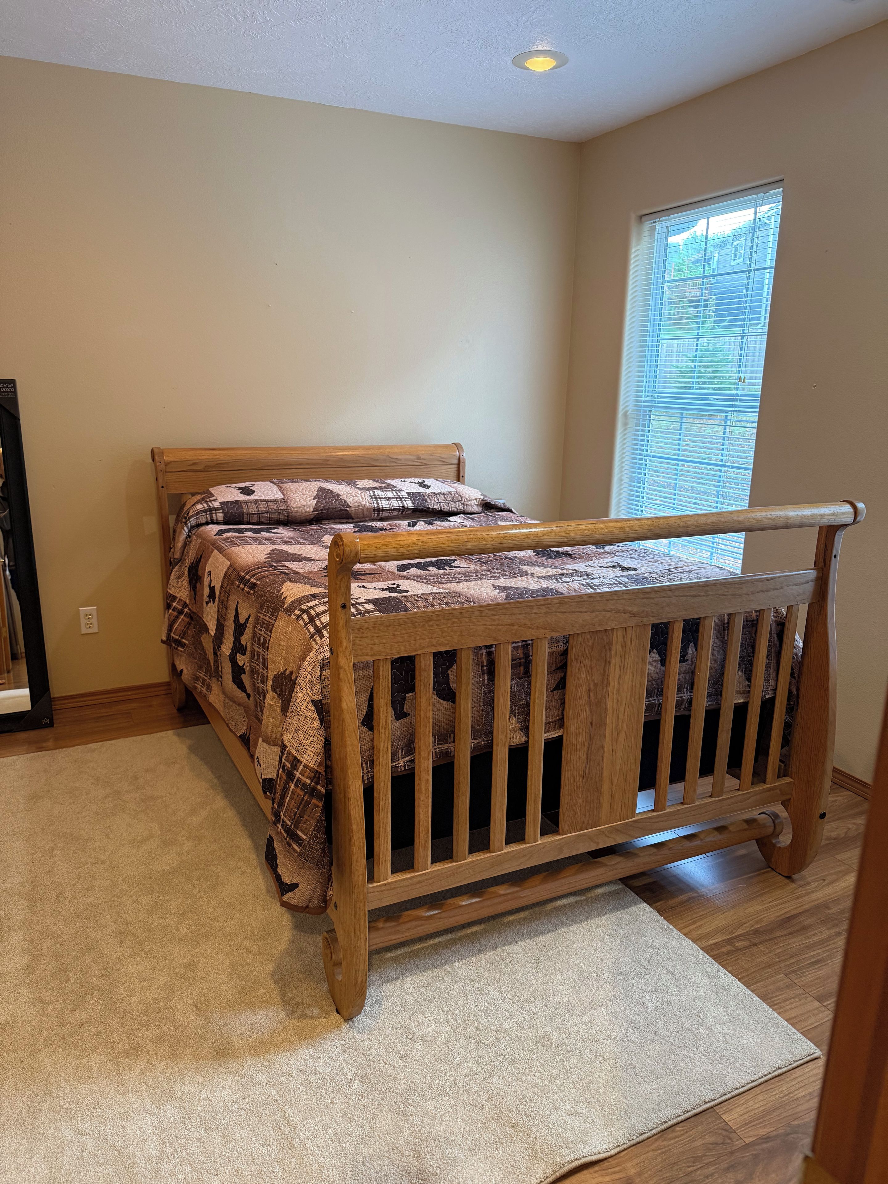 Un dormitorio con cama de madera, ventana con persianas y piso alfombrado.