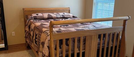 Un dormitorio con cama de madera, ventana con persianas y piso alfombrado.