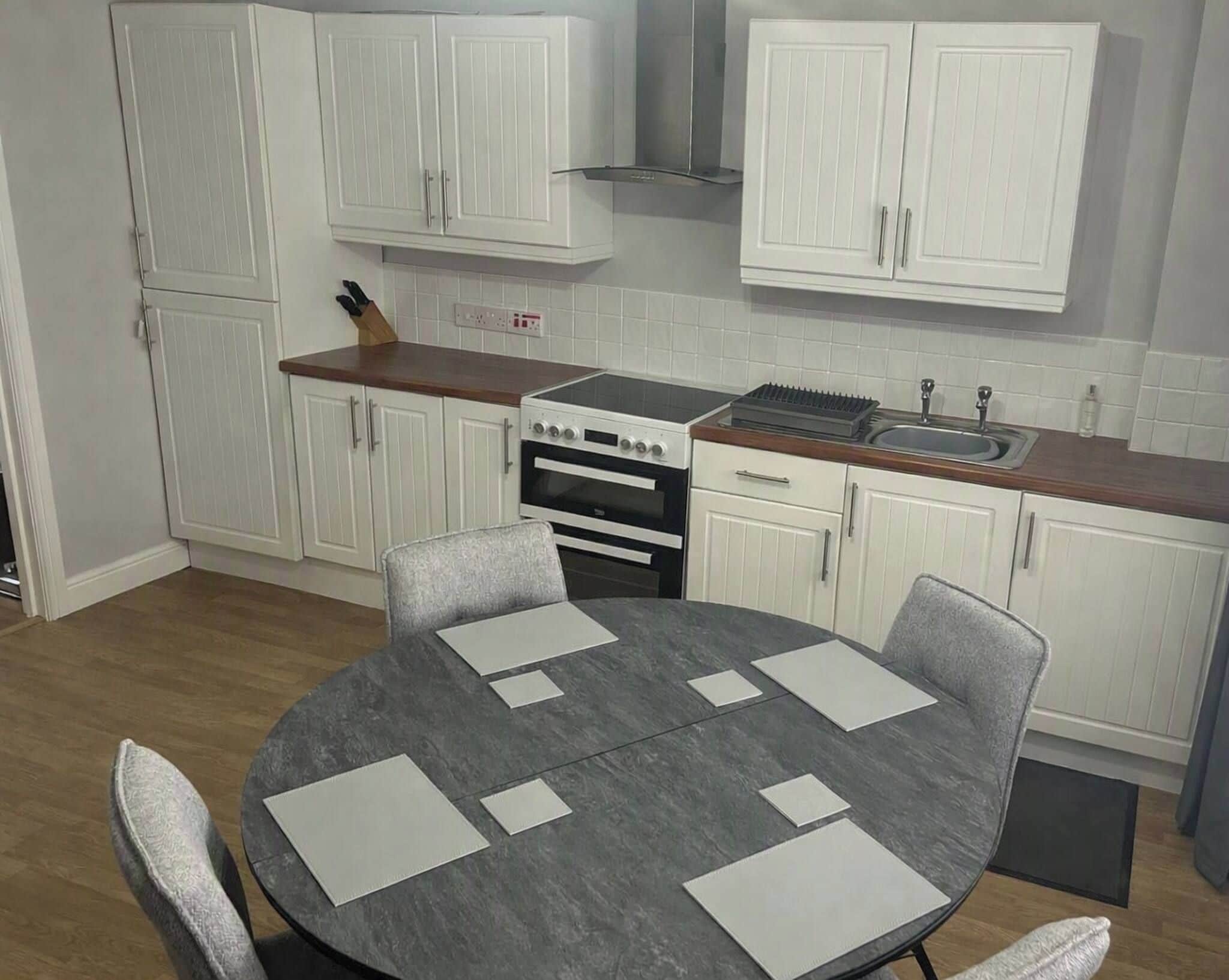 A compact kitchen with white cabinets, a stove, and a sink. There is a round table with chairs.