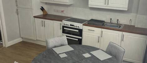 Una cocina compacta con armarios blancos, estufa y lavaplatos. Hay una mesa redonda con sillas.