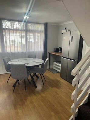 A compact living space with a dining area featuring a round table and chairs, a kitchenette with a refrigerator, and a staircase leading to an upper level. - 2 Bedroom Villa, Sleeps 5, Wifi, Parking, Beach (Dawlish)