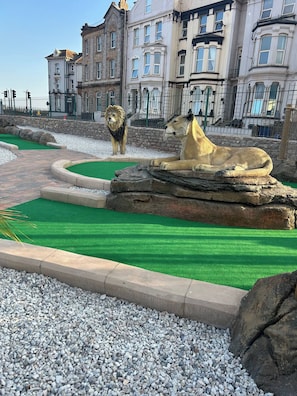 A landscaped area with a lion and a cheetah enclosure, surrounded by a stone wall and a building in the background. - 2 Bedroom Villa, Sleeps 5, Wifi, Parking, Beach (Dawlish)