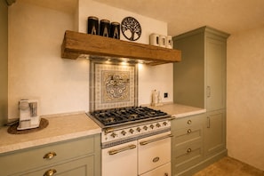 A kitchen with a gas stove, a coffee maker, and a cabinet with a decorative tile backsplash.