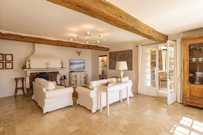 Un salon spacieux doté d’une cheminée, de meubles blancs et d’un grand plafond avec une poutre en bois.