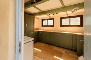 A compact kitchen with green cabinets, a white countertop, and a window with a view of trees.