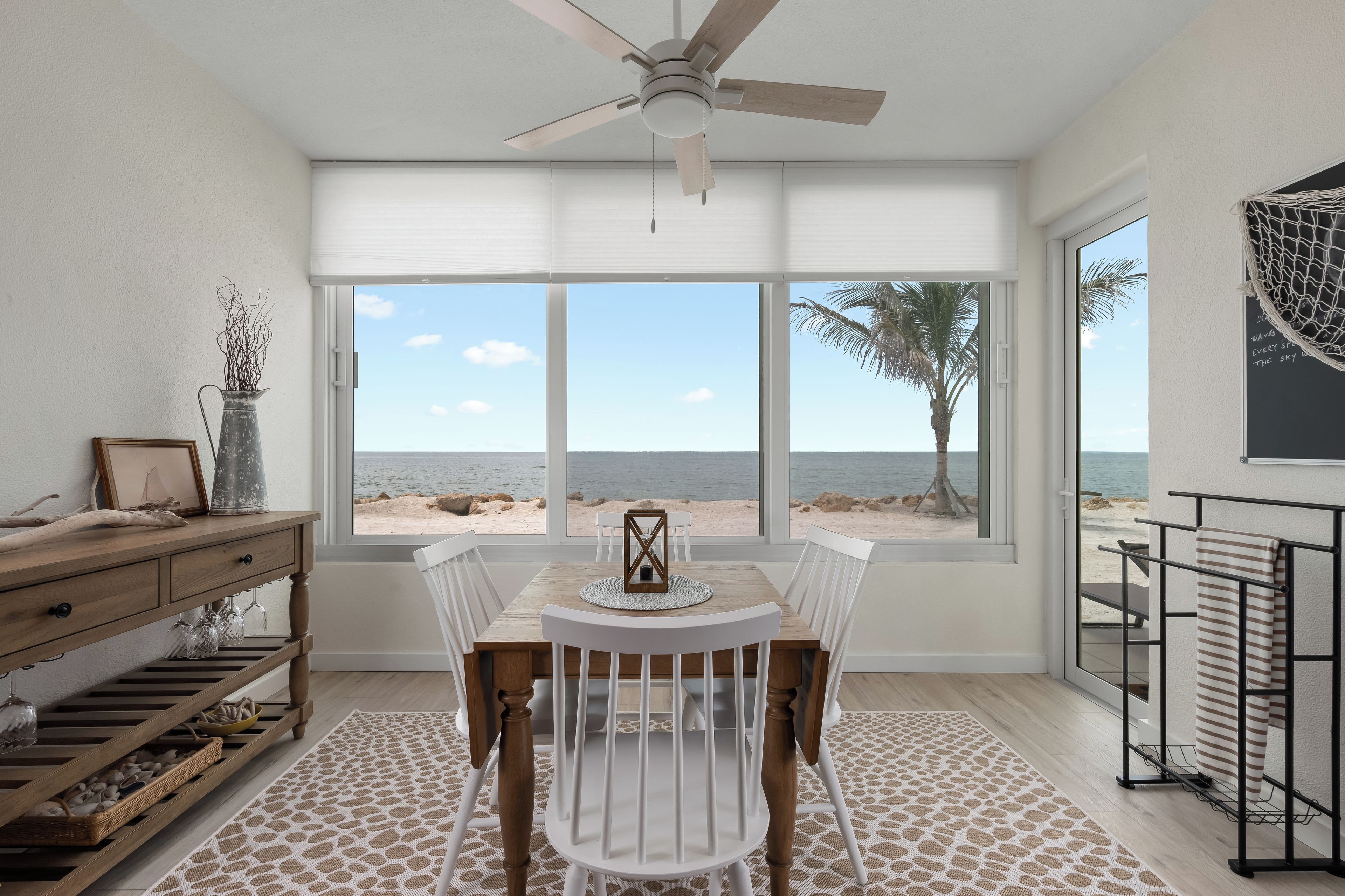 A dining area with a view of the beach, a ceiling fan, and a table with chairs.