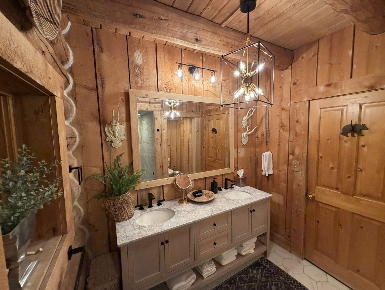 A wooden bathroom with a large mirror, two sinks, and a towel rack.