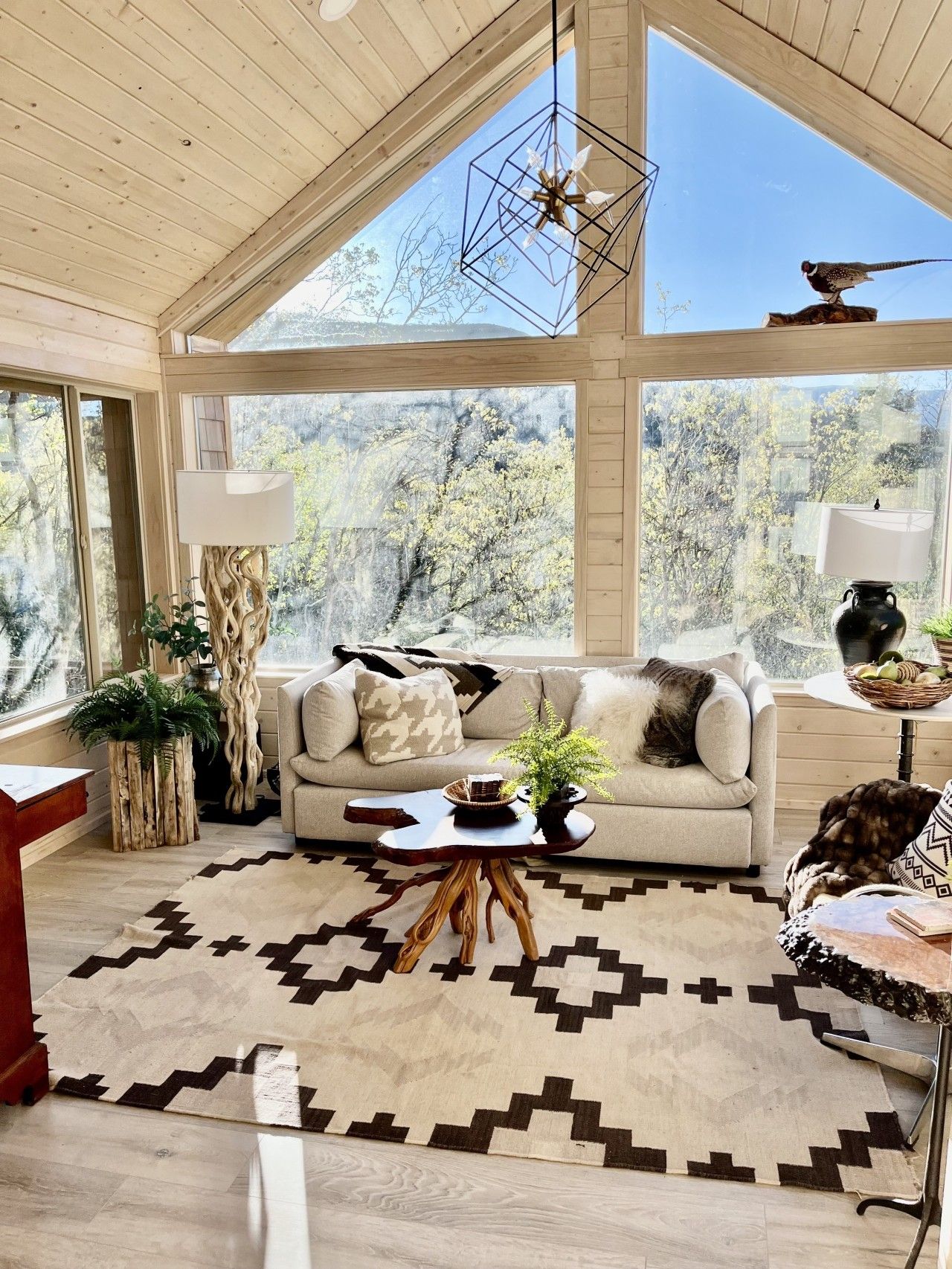 Ein geräumiges Wohnzimmer mit großem Fenster, Holzboden, moderner Pendelleuchte und einem gemusterten Teppich.