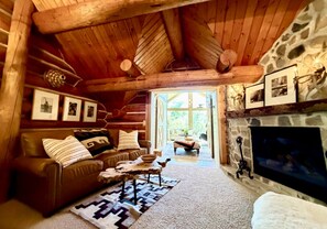 A cozy cabin interior with a stone fireplace, a leather sofa, and a rustic wooden ceiling. - A Sundance Original • Historic Log Cabin (Sundance)