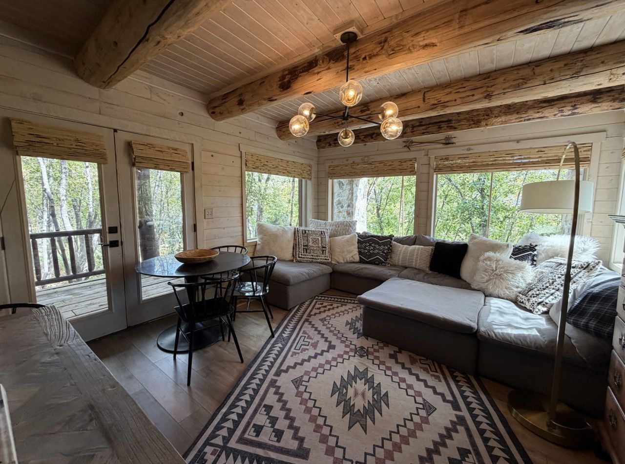 A cozy cabin interior with a dining area, a sofa set, and a patterned rug.