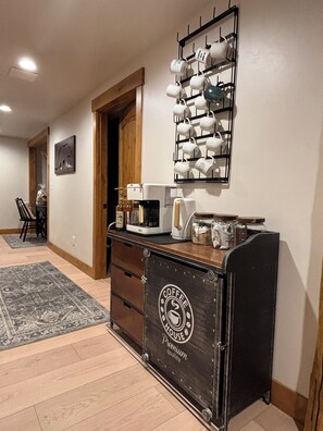 A kitchen area with a coffee station, a coffee maker, a toaster, and a mug rack on the wall.