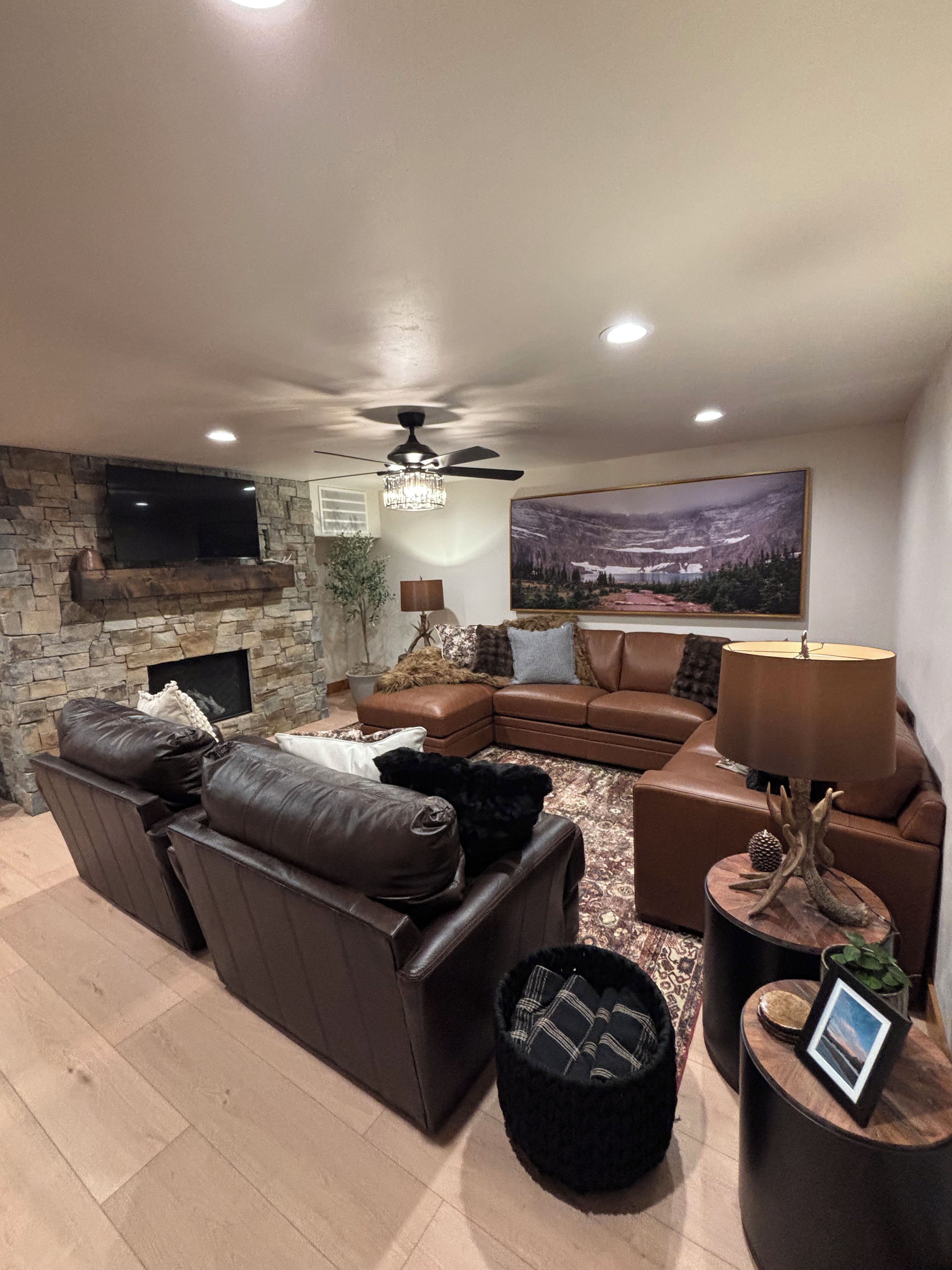 A living room with a stone fireplace, leather sofas, a flat-screen TV, and a large landscape painting.