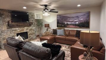A living room with a stone fireplace, leather sofas, a flat-screen TV, and a large landscape painting.