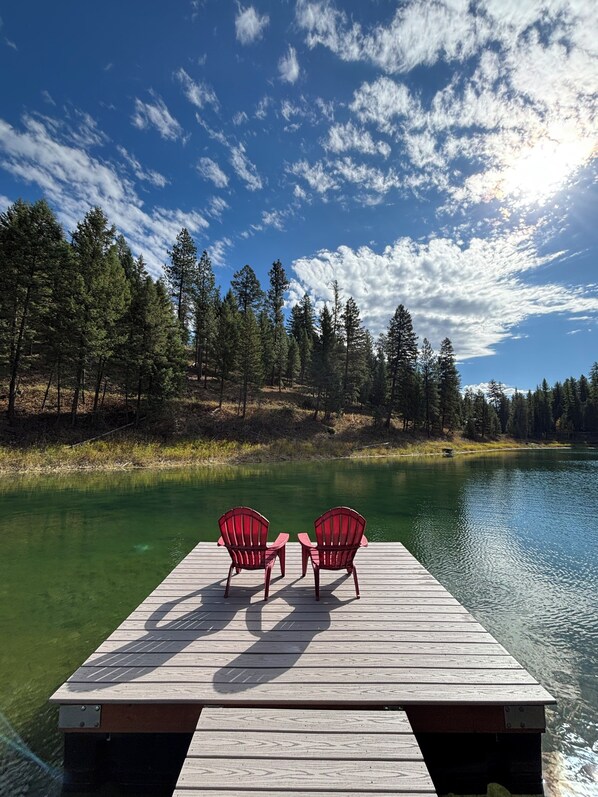A wooden dock extending into a lake with two red Adirondack chairs facing the water.