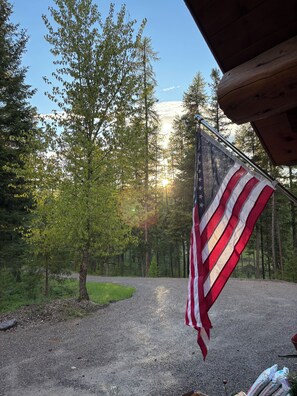 An American flag on a flagpole in a forested area with a gravel path.
