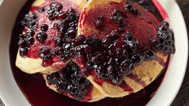 Eine Schüssel Pfannkuchen mit Blaubeeren und Ahornsirup, inklusive Löffel.
