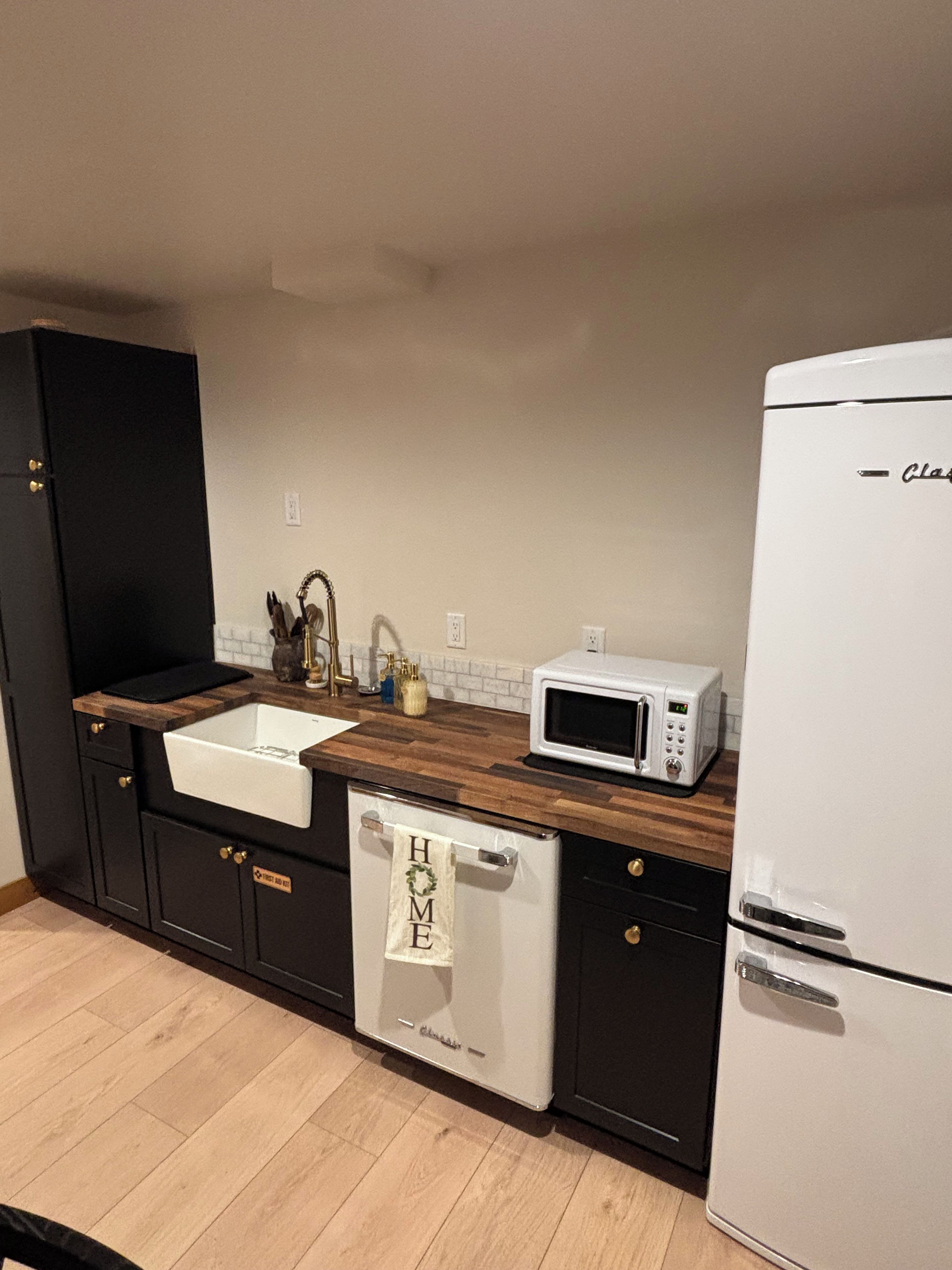 A kitchen with a white dishwasher, a white refrigerator, a microwave, and a wooden countertop.
