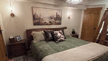 A bedroom with a bed, a ceiling fan, a painting, a wooden door, and a nightstand.