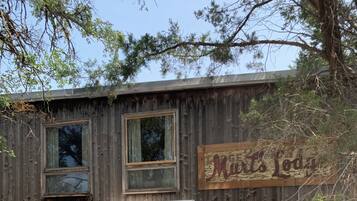 Un edificio de madera rústico con un letrero que dice 'Mats Lodge'. Hay una silla verde y una mesa con sillas afuera.