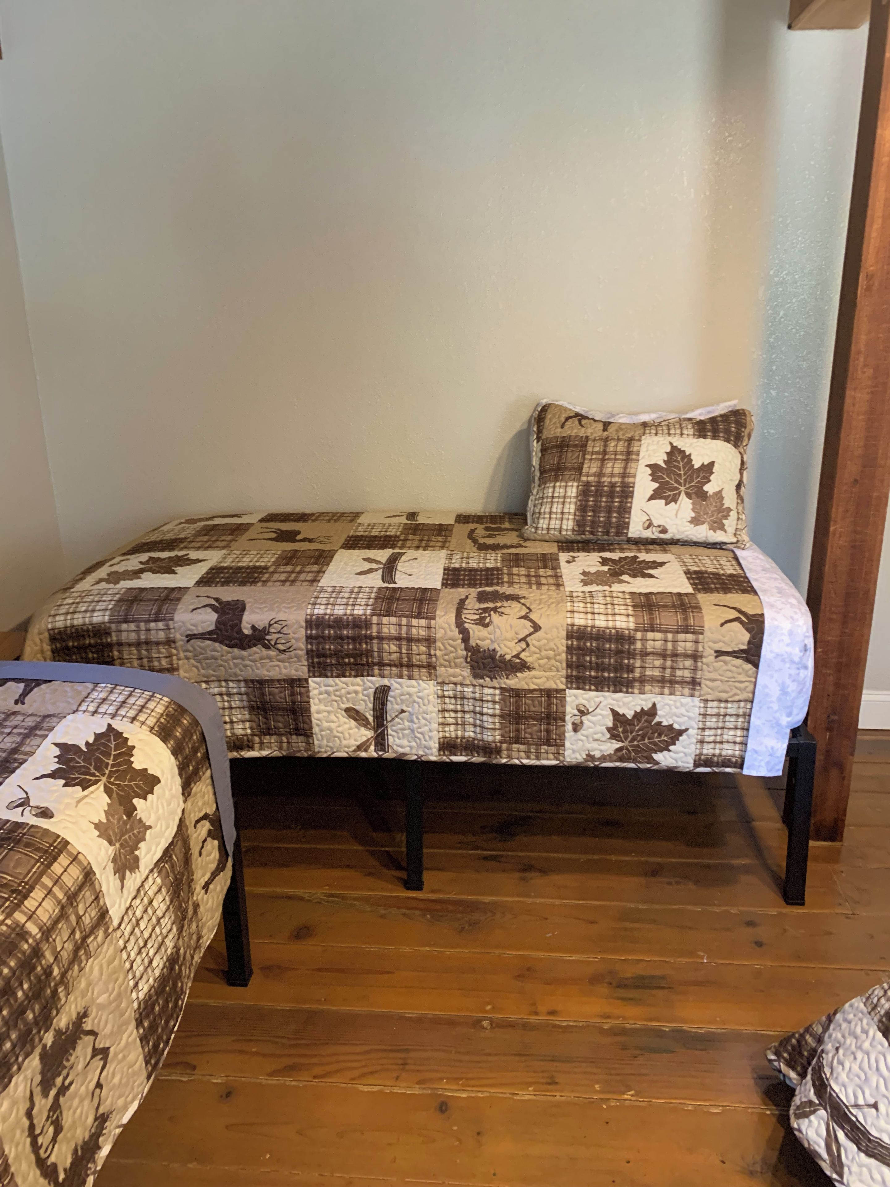 A single bed with a quilted headboard and footboard, a matching pillow, and a wooden floor.