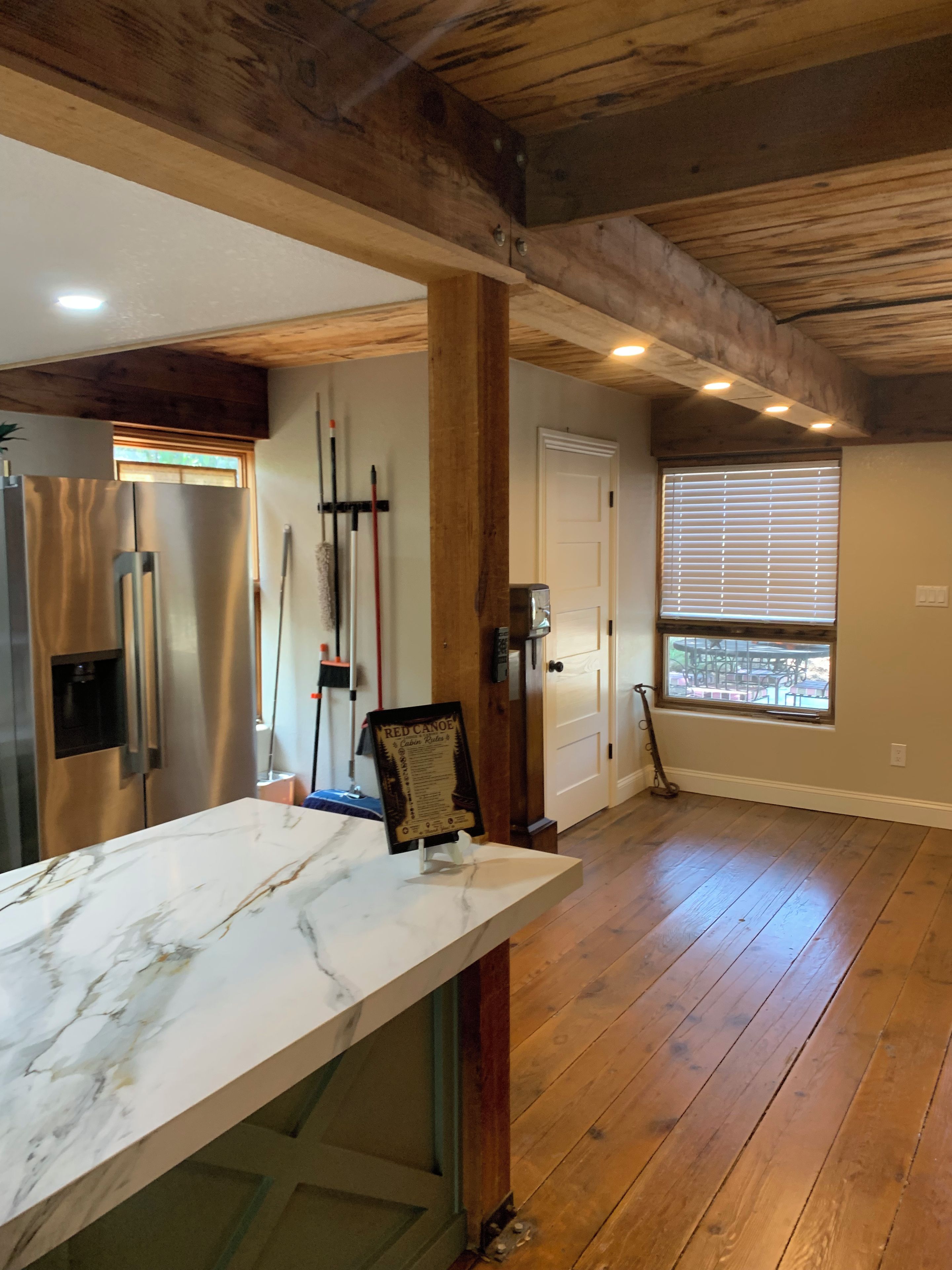 A spacious kitchen with a marble countertop, wooden beams, and a view through a window.