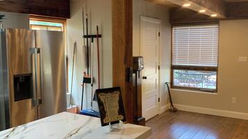A spacious kitchen with a marble countertop, wooden beams, and a view through a window.