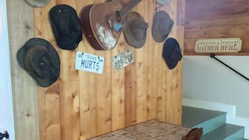 Un mur en bois orné de divers chapeaux et d’une guitare, une table avec des chaises, et une pancarte sur laquelle on peut lire : « C’est ici que se réunissent amis et famille ».