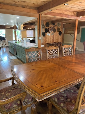 A wooden dining table with ornate chairs, a kitchen in the background, and a sign on the wall. - Murt’s Lodge at Red Canoe Lodge Historic Lake Whitney Resort, Totaly Reimagined (Clifton)