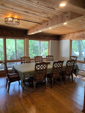 A dining area with a wooden table and chairs, large windows with a view of trees, and a chandelier.