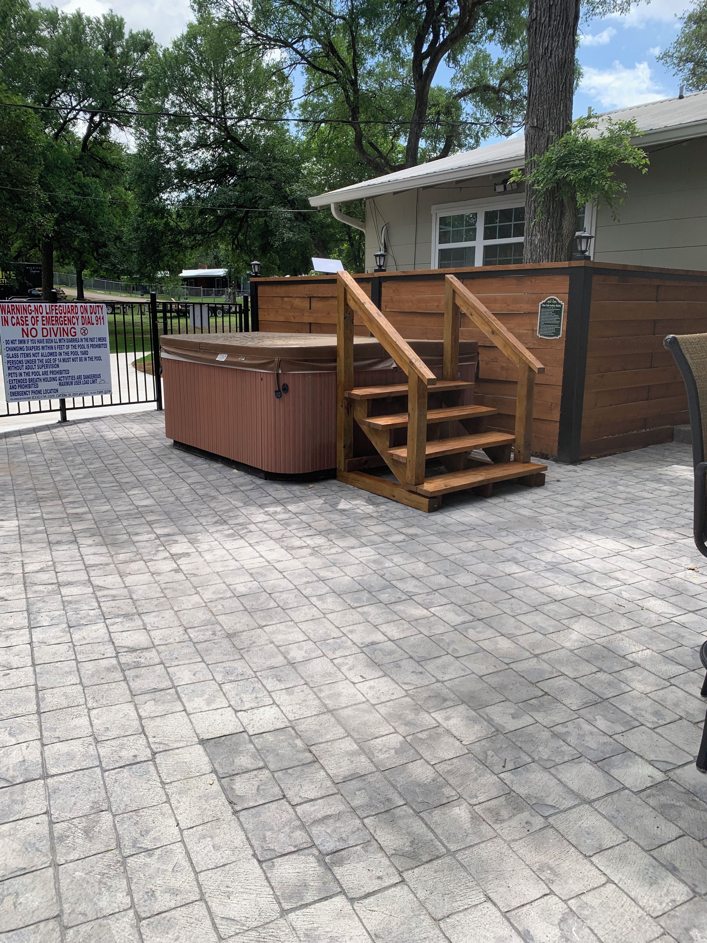 A hot tub with wooden steps leading up to it, surrounded by a wooden fence and a brick patio.