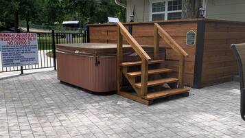 A hot tub with wooden steps leading up to it, surrounded by a wooden fence and a brick patio.