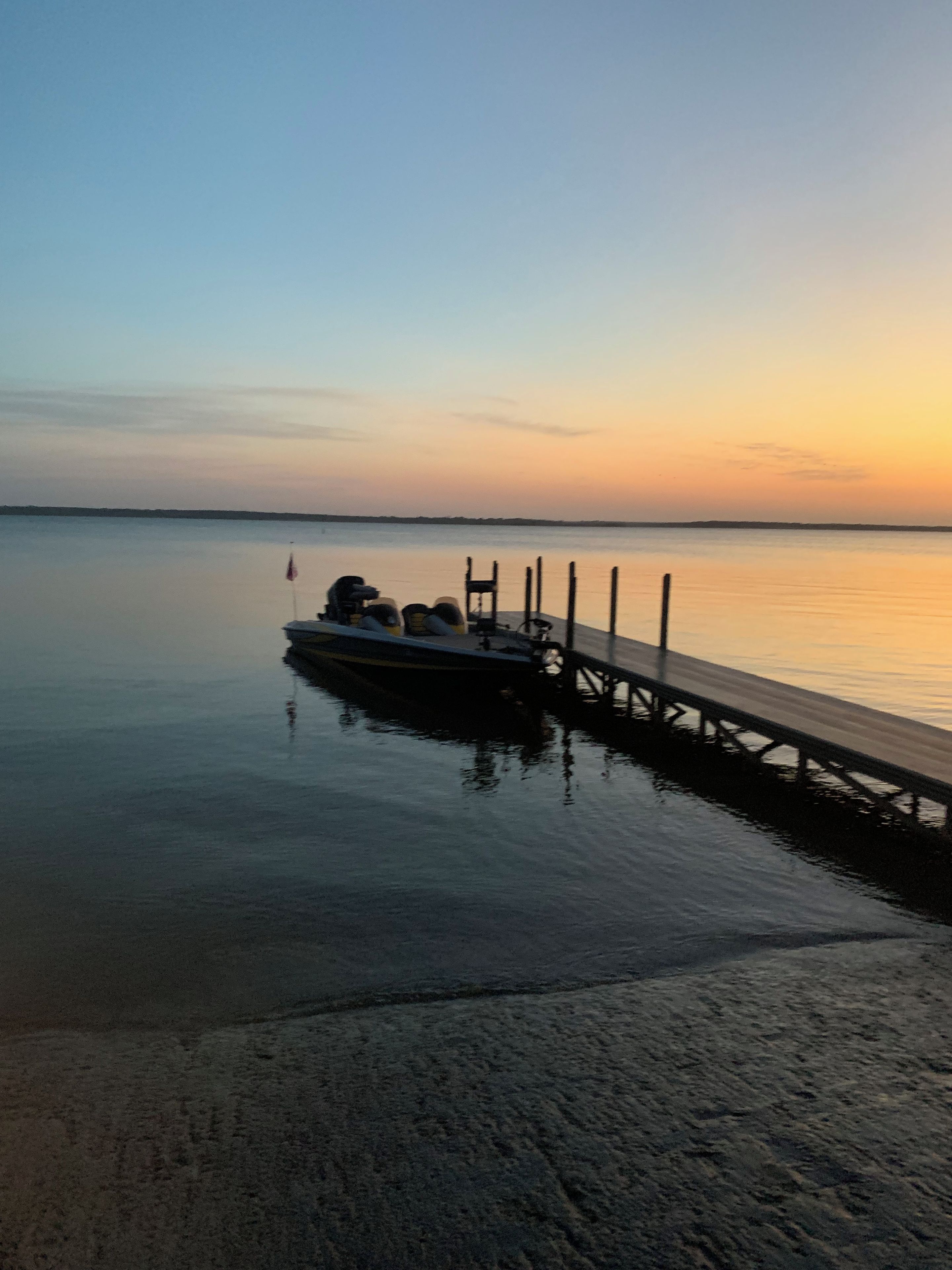 A calm body of water with a dock extending into it, a boat moored at the dock, and a clear sky above.